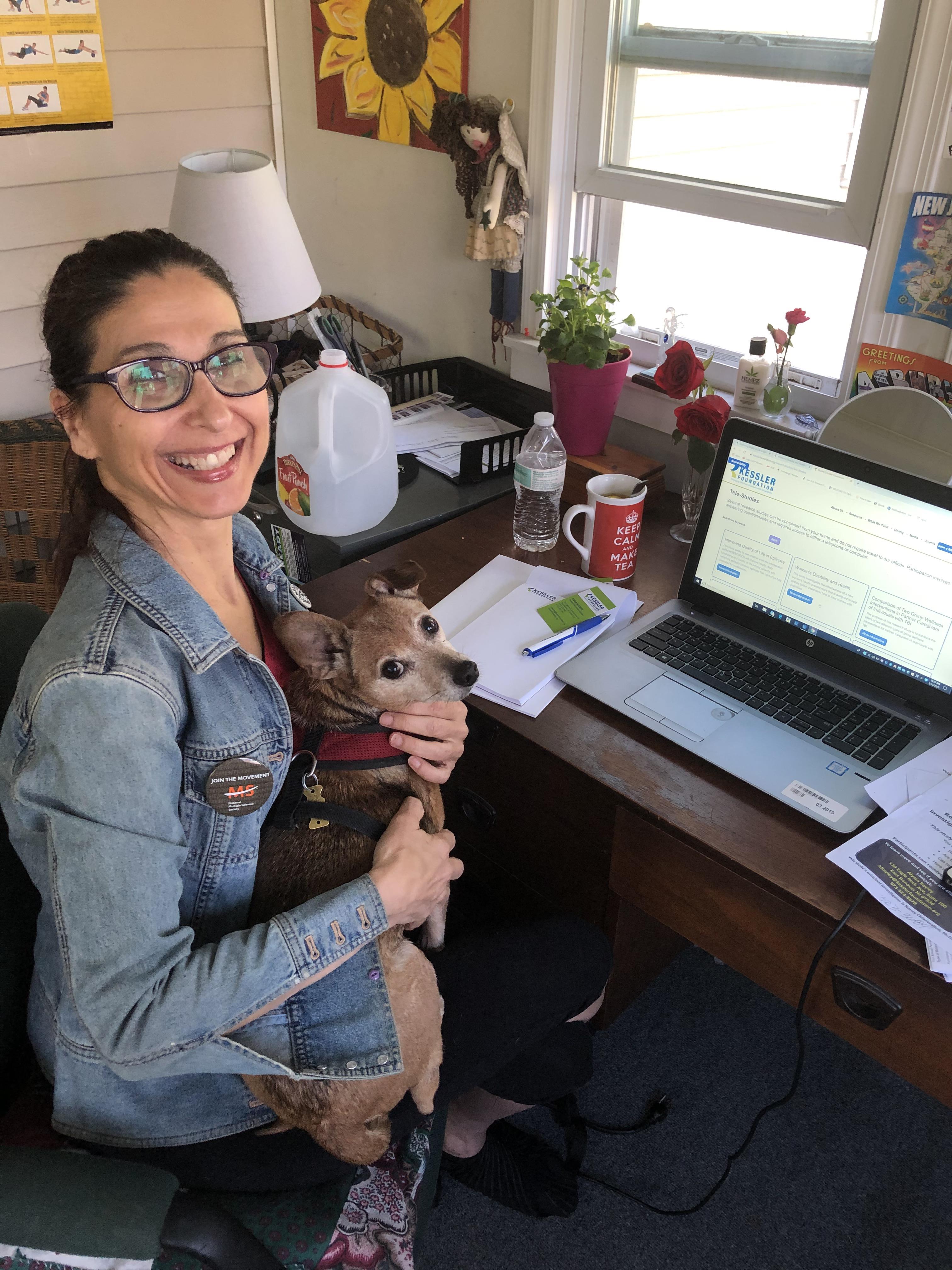 Carla Basante holding her dog, smiling at the camera, and working from home 