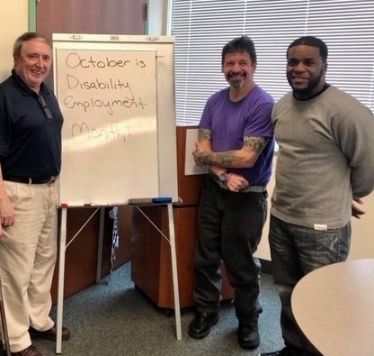 Three men smiling and standing next to a white board with text 