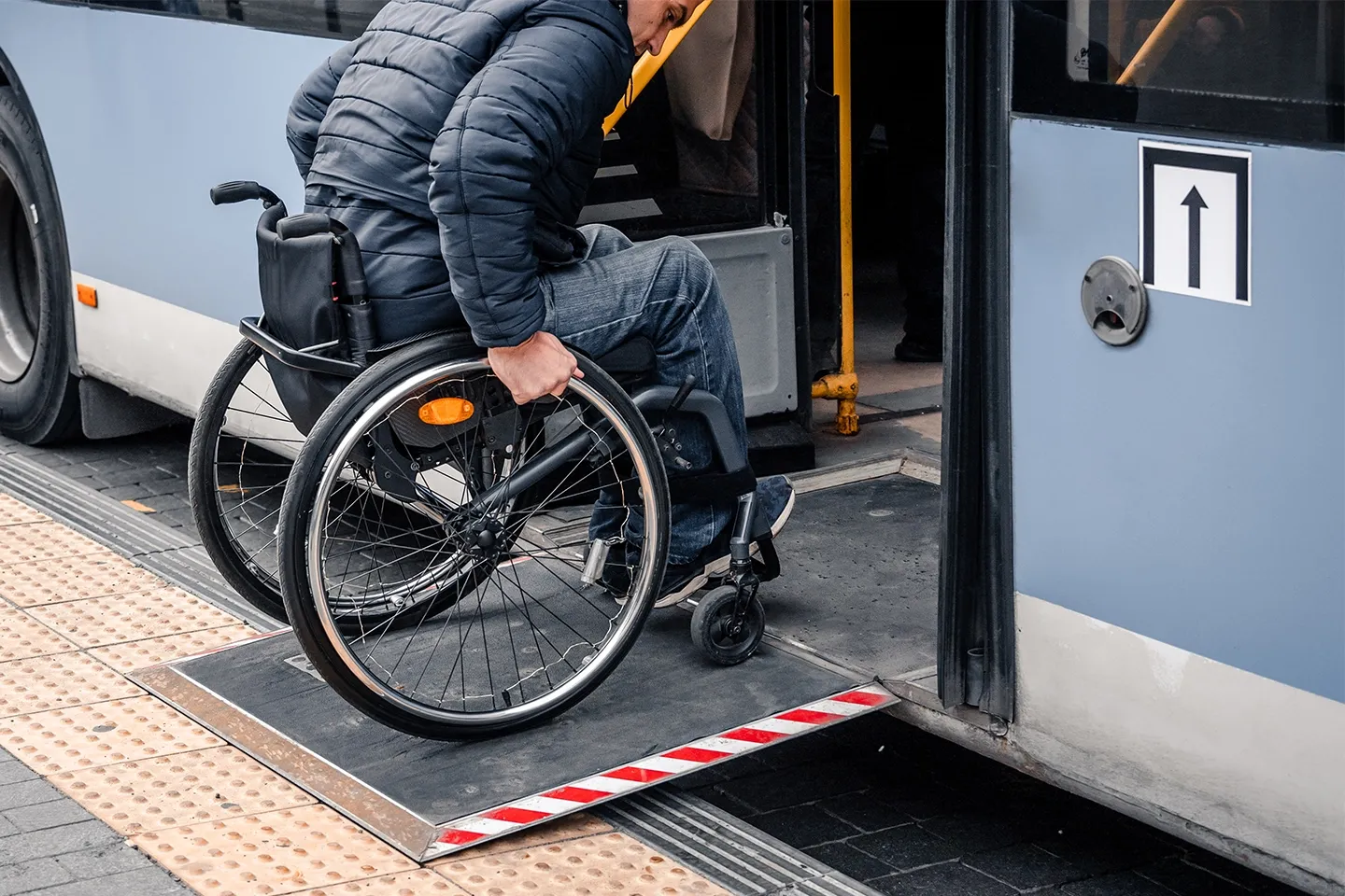 Person with a physical disability enters public transport on an accessible ramp.