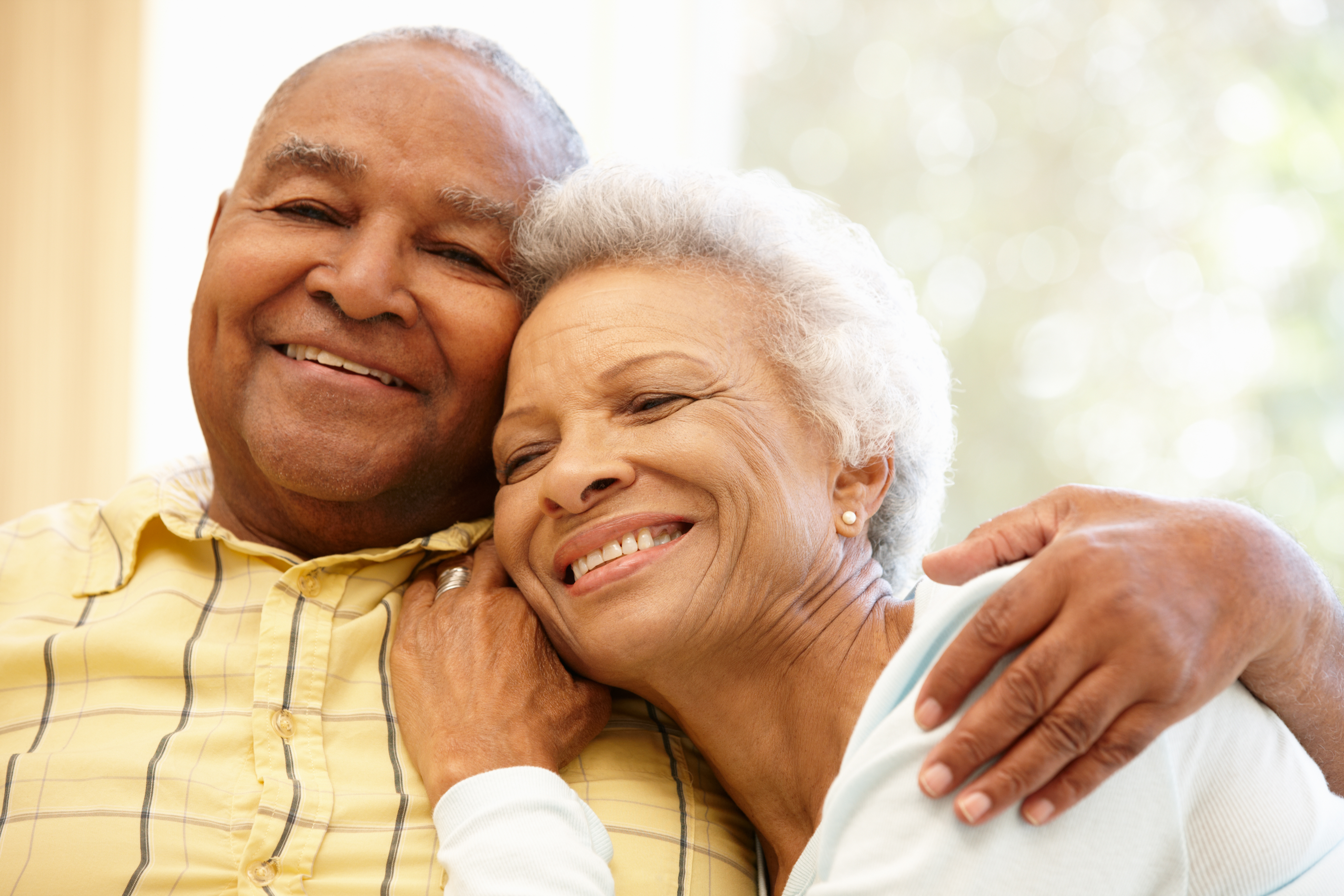 Close-up of an older couple embracing in a bright, softly lit room, symbolizing security and peace of mind through estate planning and charitable giving. 