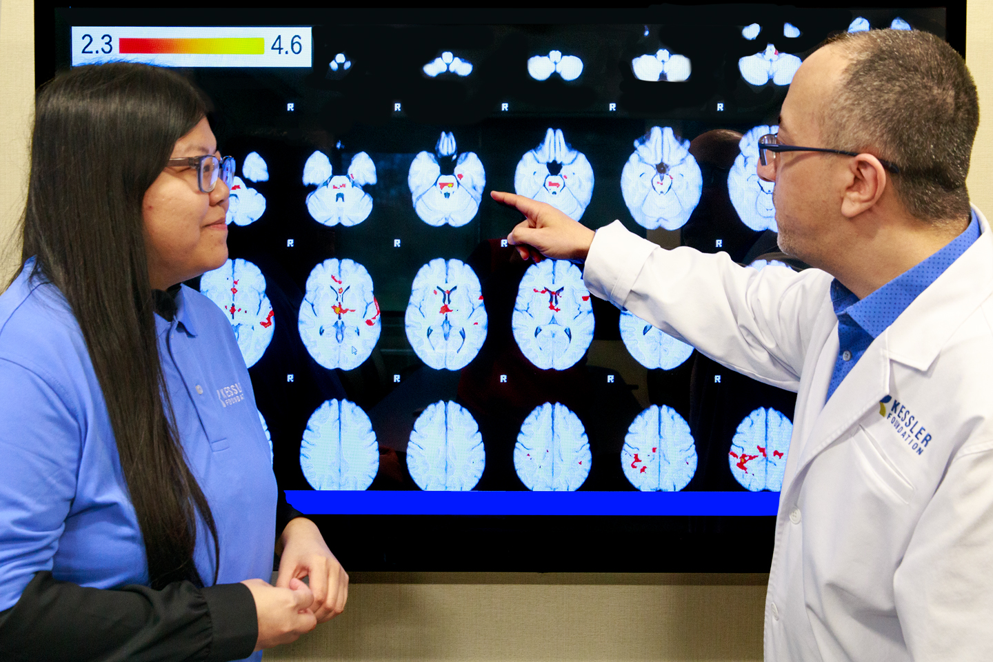 Anthony Lequerica, PhD, is pointing to a large screen showing traumatic brain injury MRI brain scans. Tien Tong, PhD is standing to the left of him.