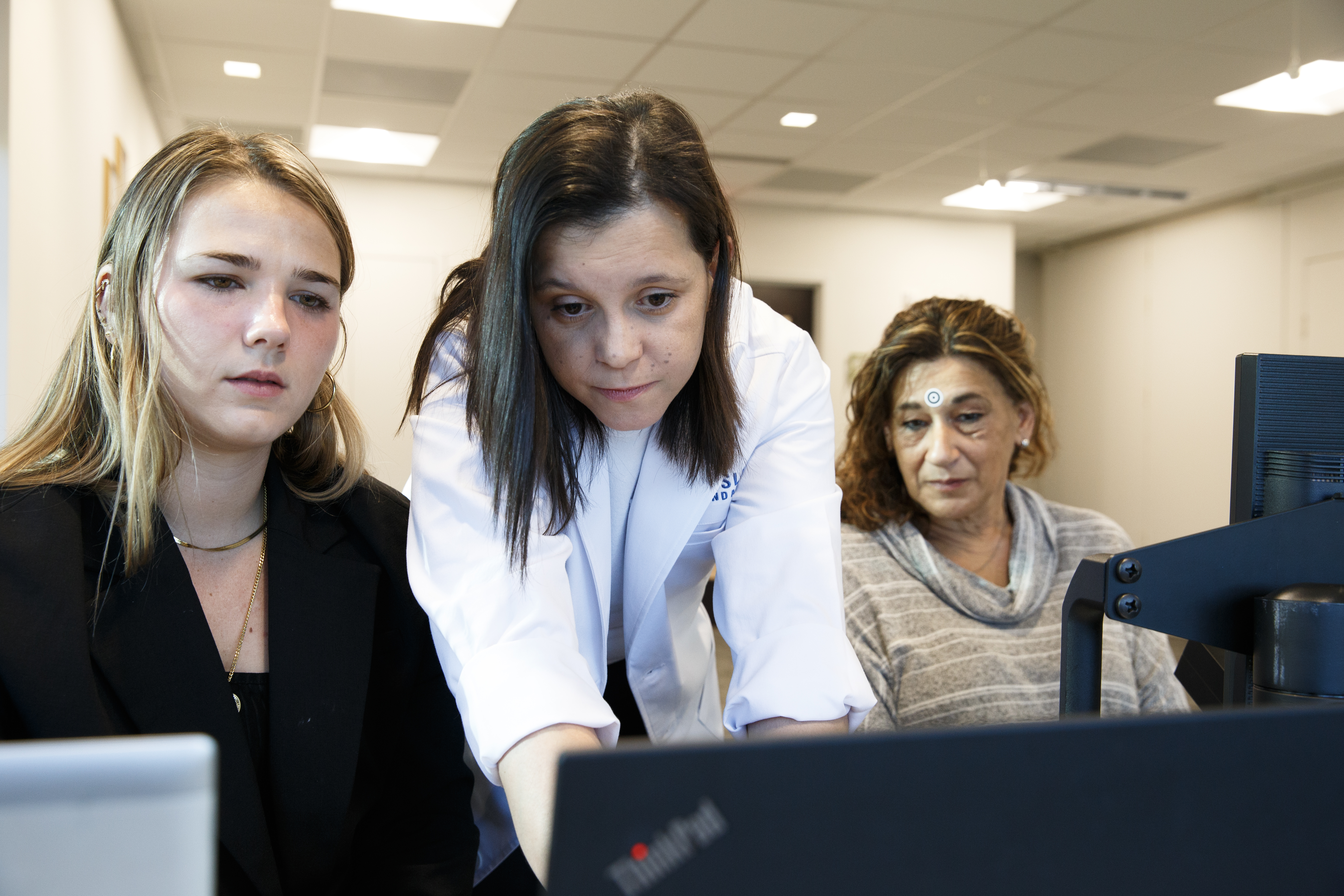 Collaborative MS research discussion at Kessler Foundation with a clinician reviewing data on a laptop alongside colleagues, highlighting the latest multiple sclerosis insights and evidence-based advances 