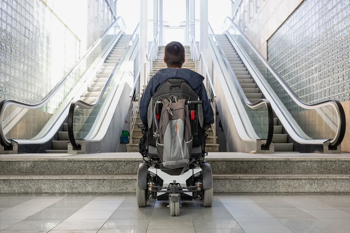 Man with disability in wheelchair stopped in front of staircase, raising awareness of architectural barriers and accessibility issues.