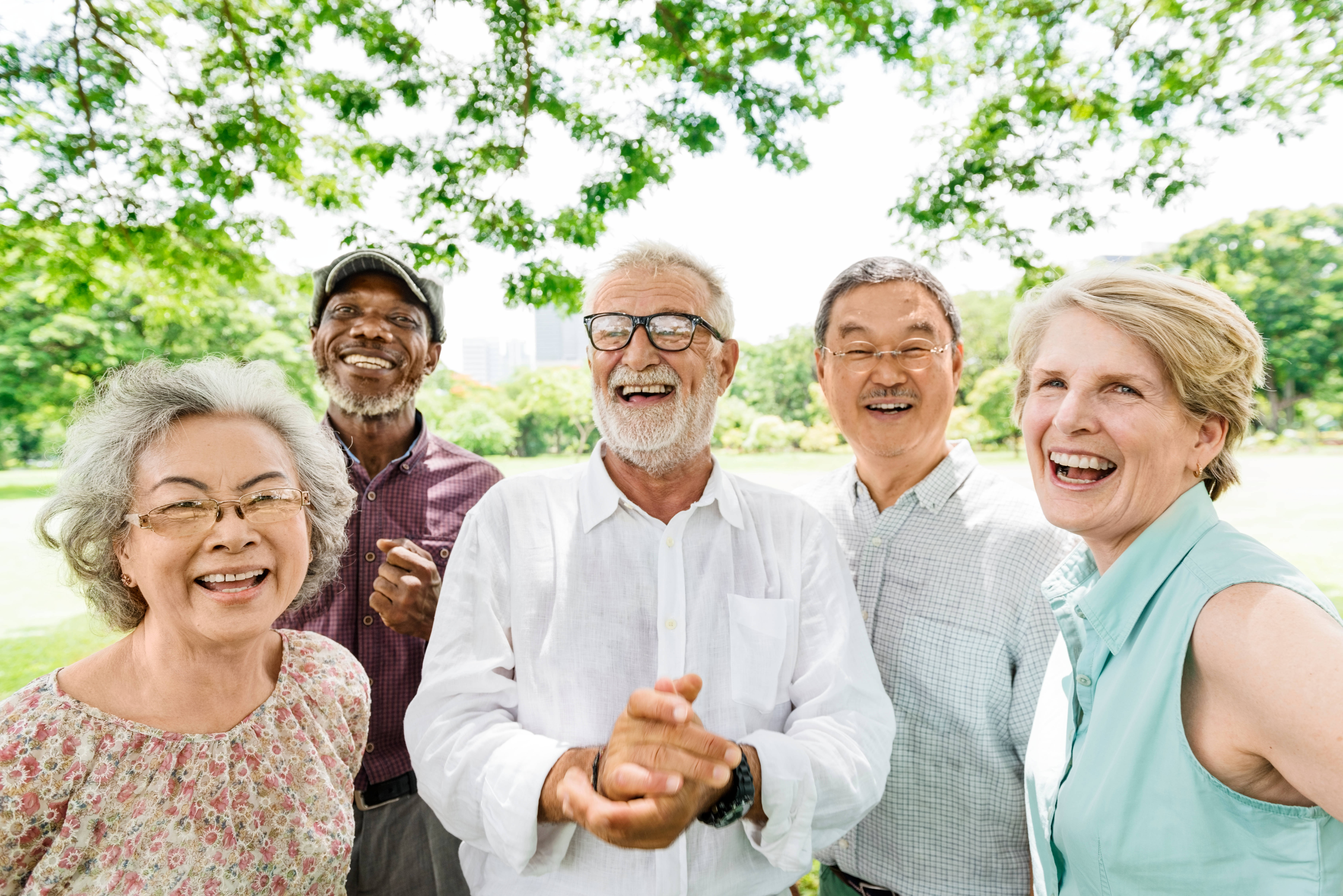 A small group of adults standing close together outdoors, smiling and posing for a group photo with trees and greenery in the background.