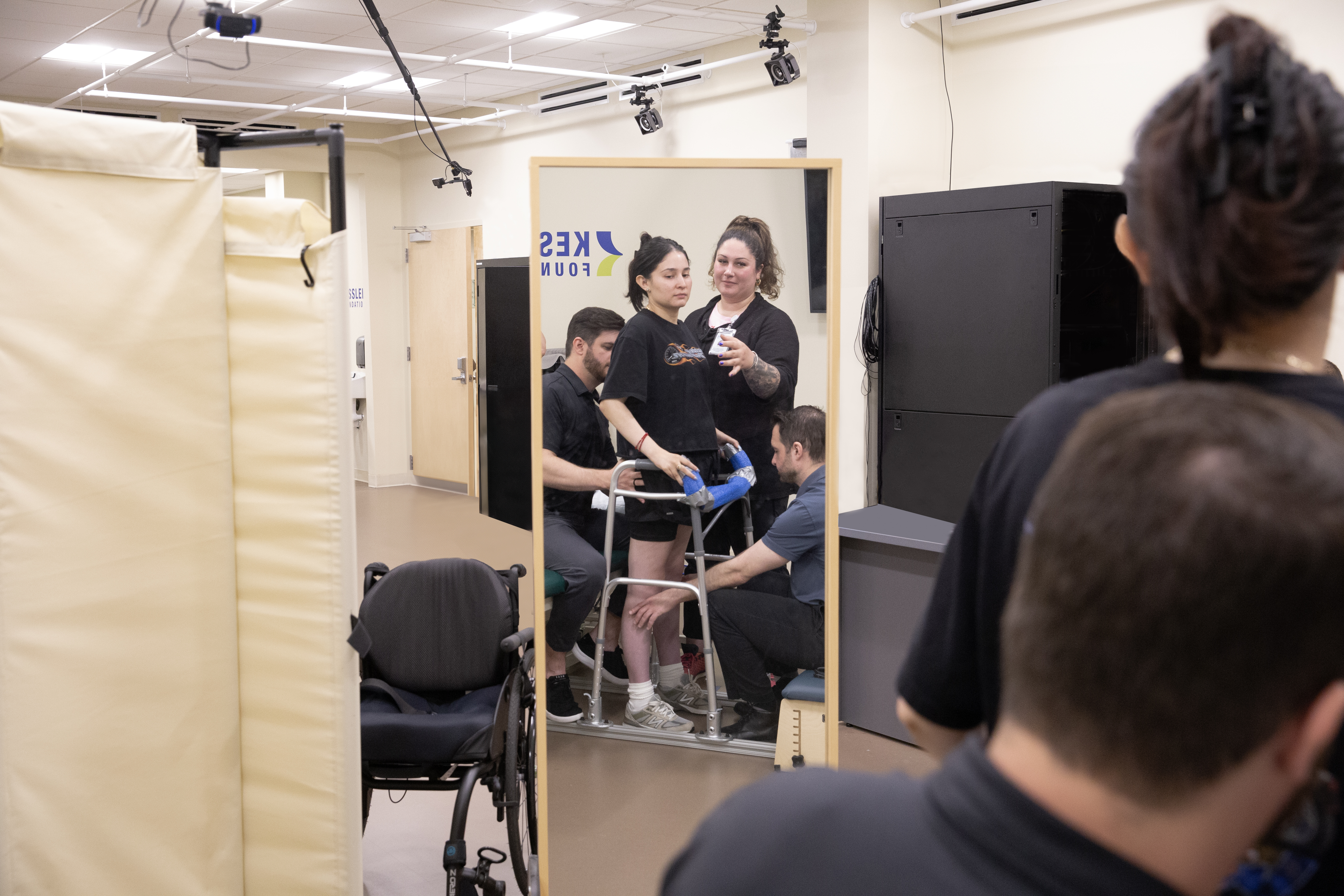 A woman stands assisted during a rehab setting