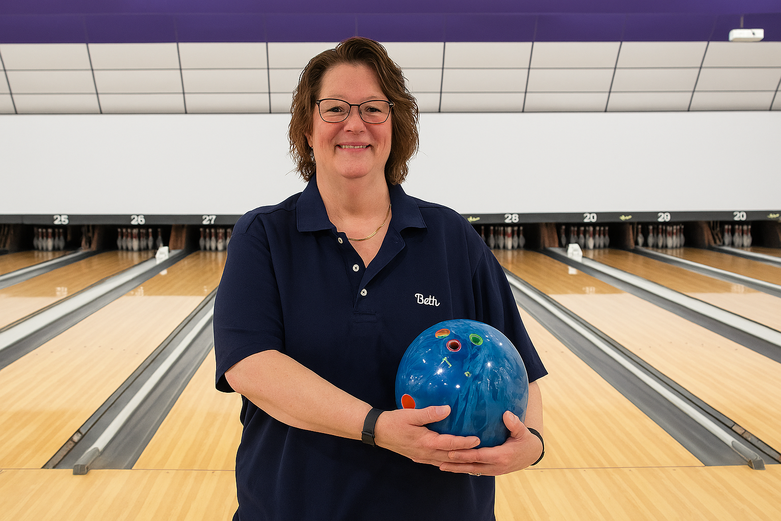 Person standing at a bowling lane holding a blue bowling ball, with polished lanes and pins visible in the background.