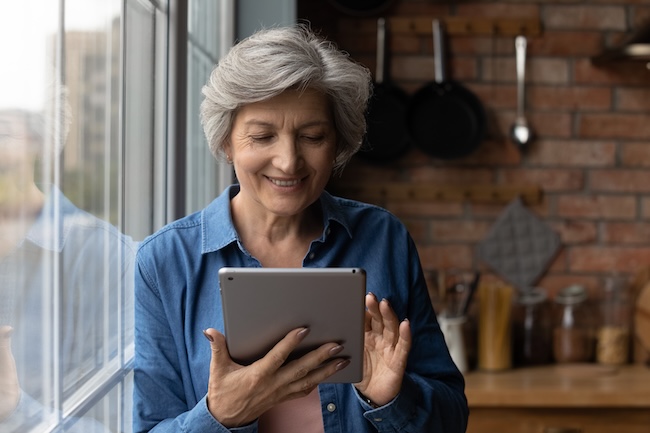 Individual using a digital tablet near a bright window, representing participation in a multiple sclerosis research study through online enrollment. 