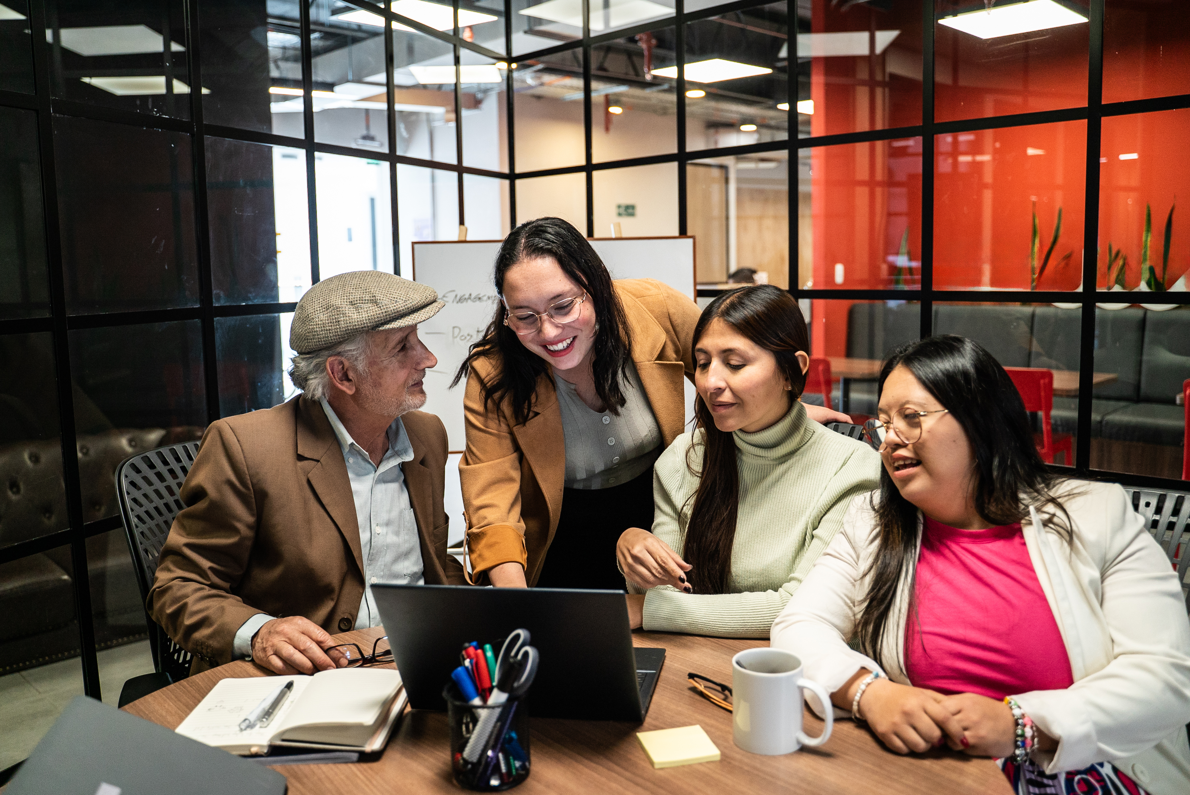Diverse team gathered around a table in a meeting, reviewing documents and a laptop during a collaborative discussion.