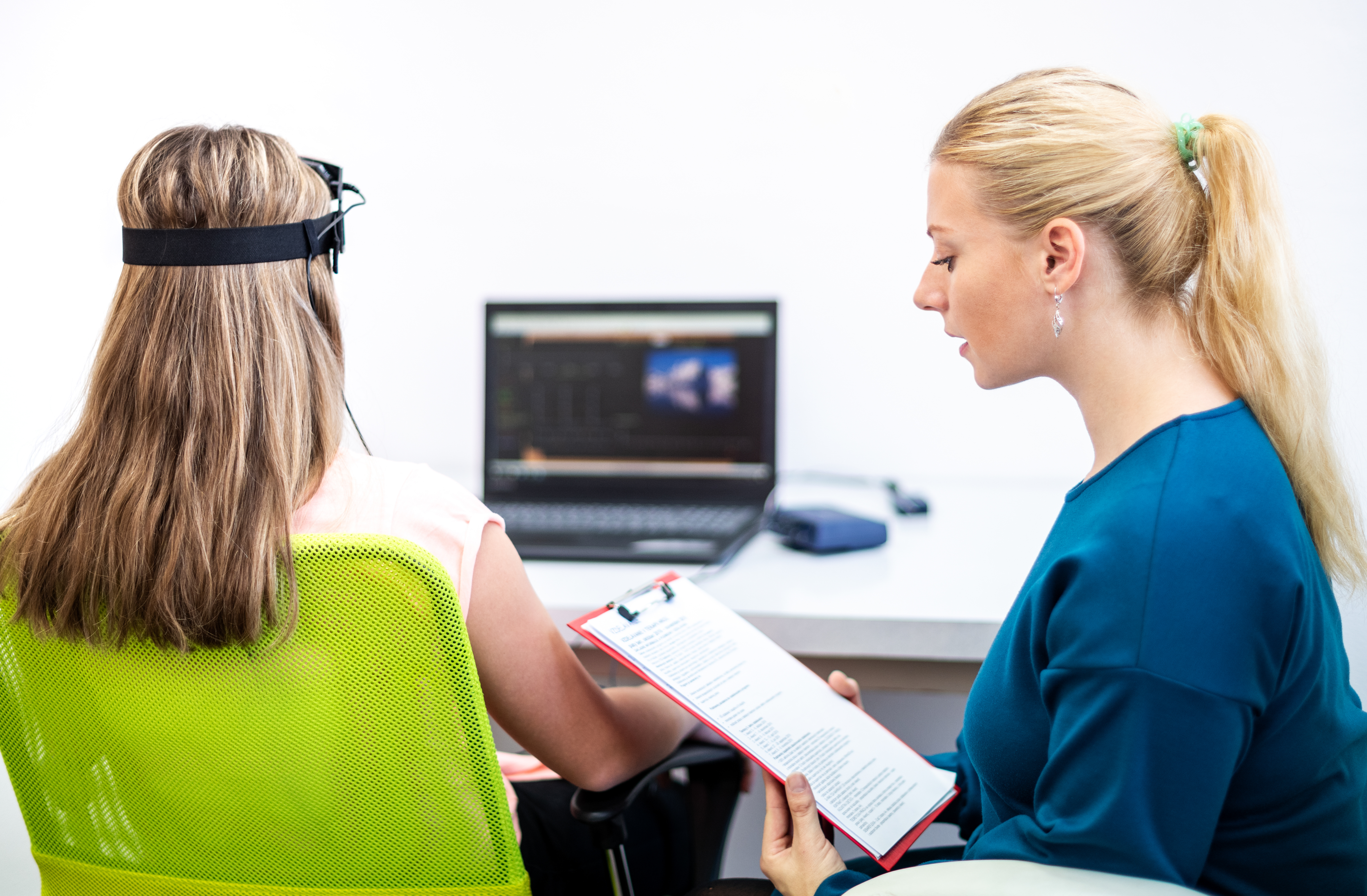 Person sits in a clincial setting wearing a headset with a clinician reviewing data