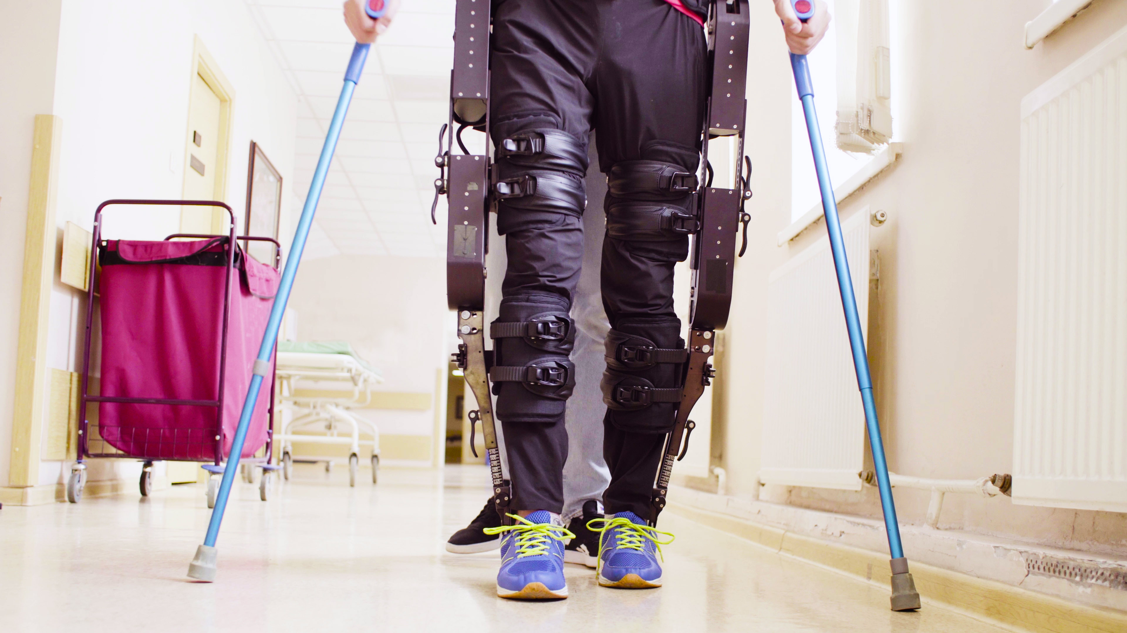 A person stands using crutches and a robotic exoskeleton for mobility purposes