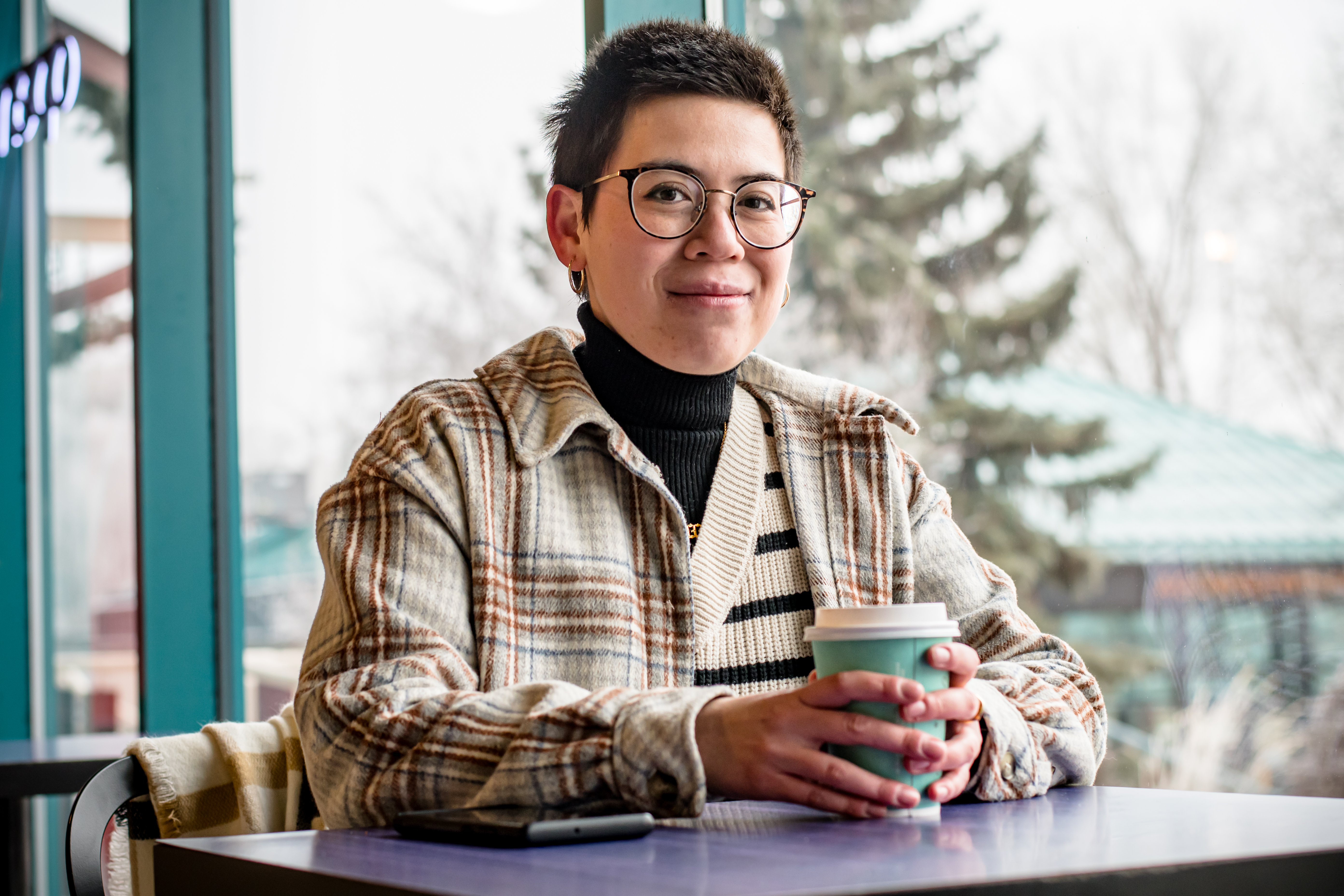 A woman sits at a table with a to-go style coffee cup and smiles