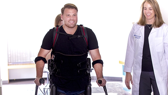 Karen Nolan, PhD walking with a participant using robotics to aid him in walking
