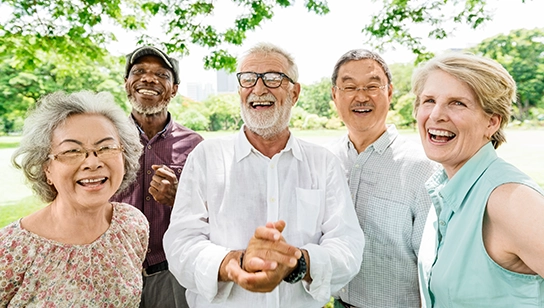 A small group of adults standing close together outdoors, smiling and posing for a group photo with trees and greenery in the background.