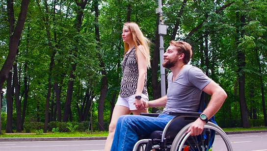 A couple holds hands while on a stroll in nature. The man is using a wheelchair.