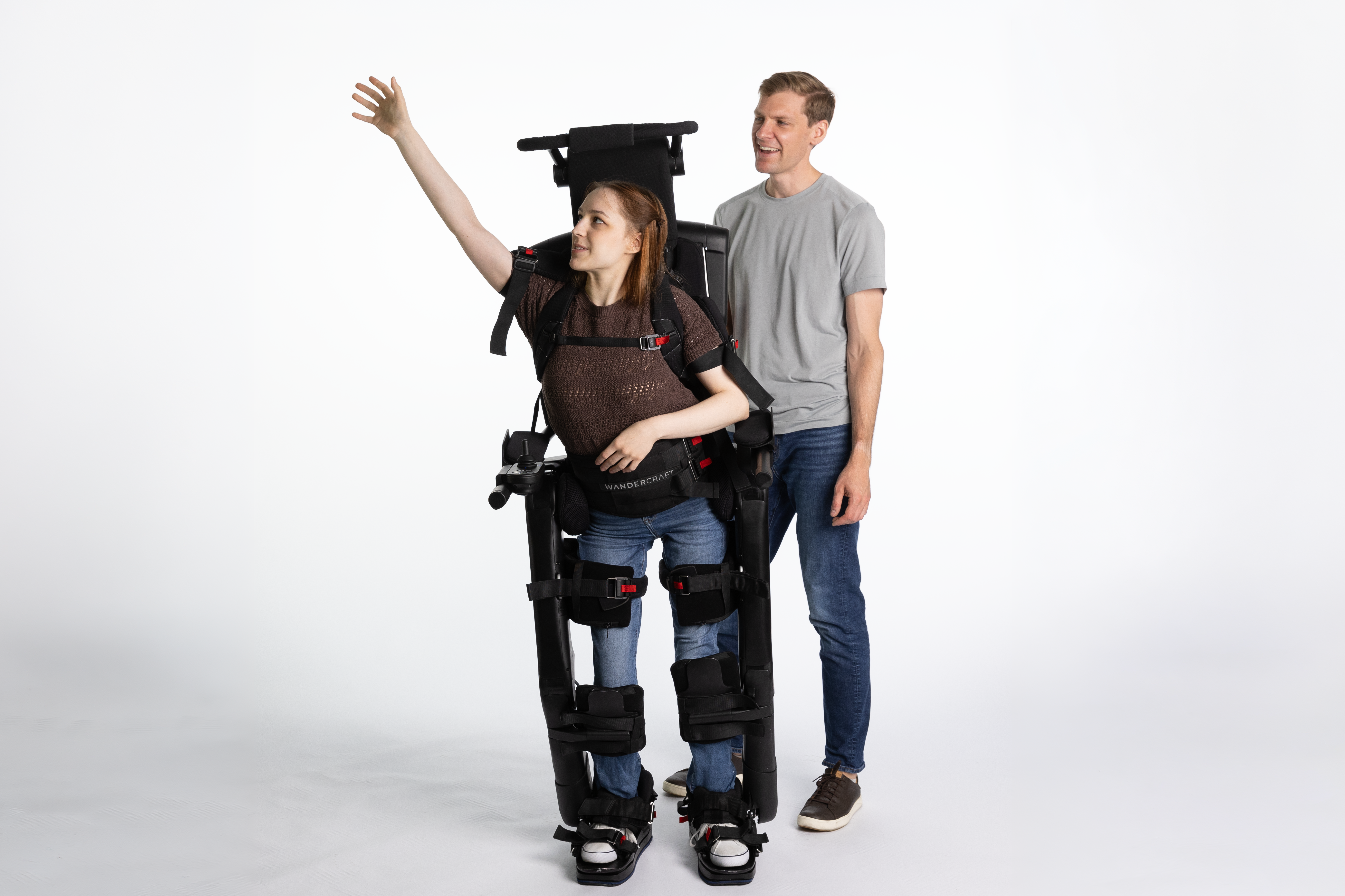 A photo of a woman using Eve™, the first self-balancing personal exoskeleton for eligible wheelchair users. A man in a gray shirt and jeans stands behind her.