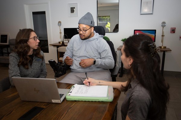 SCI Navigator Program participant Louis Ayala, center, dressed in gray sweats and a gray hat, speaks to two program navigators, Emily DeBel (left), and Samantha "Sam" Rodimer (right).