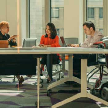 Three person sitting in a conference room, inclusion of a wheelchair user in an office setting.