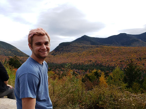 A young man standing outdoors with a beautiful landscape behind  