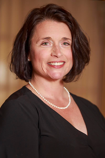 Light skin woman with dark brown hair wearing a black blouse and white pearl necklace