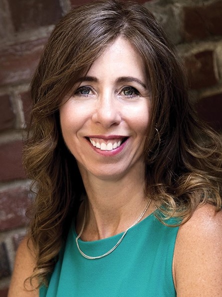 image of a lady smiling, with brown hair and a green shirt