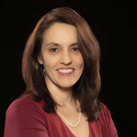 Woman wearing a red blouse, pearl necklace, and earings. 