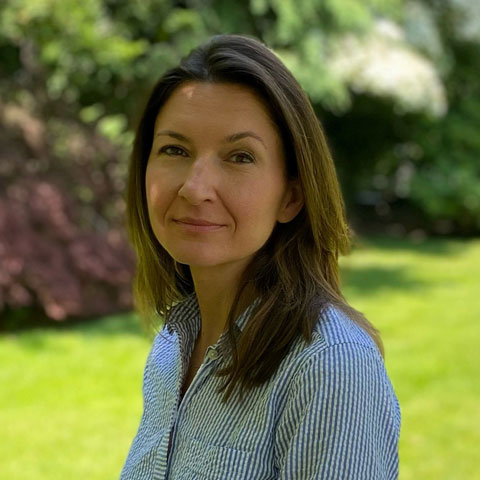 woman with light brown hair at a park wearing a blue/white pin stripe shirt