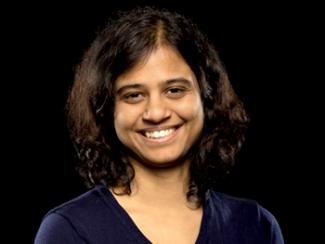 Scientist wearing a navy blue blouse smiling for the camera with a black background