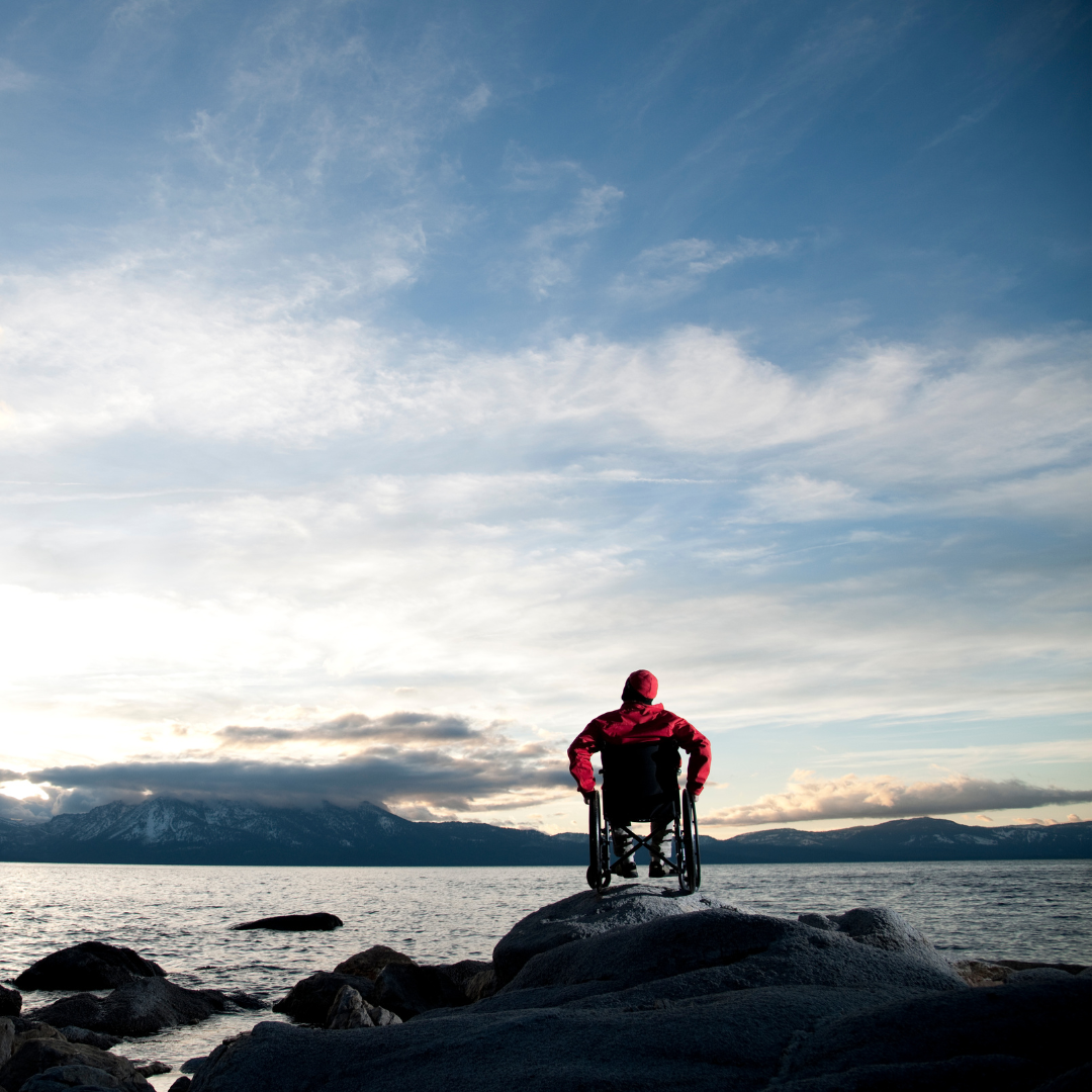 A man in a wheelchair facing the ocean and sunrise