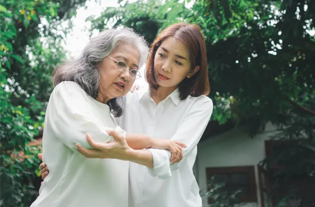 Two Asian woman, younger one holding arm of older one to help her walk