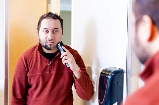Man with spatial neglect looking in a mirror and shaving only one side of his beard.