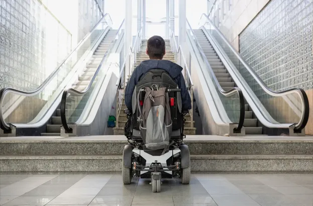 Man with disability in wheelchair stopped in front of staircase, raising awareness of architectural barriers and accessibility issues.