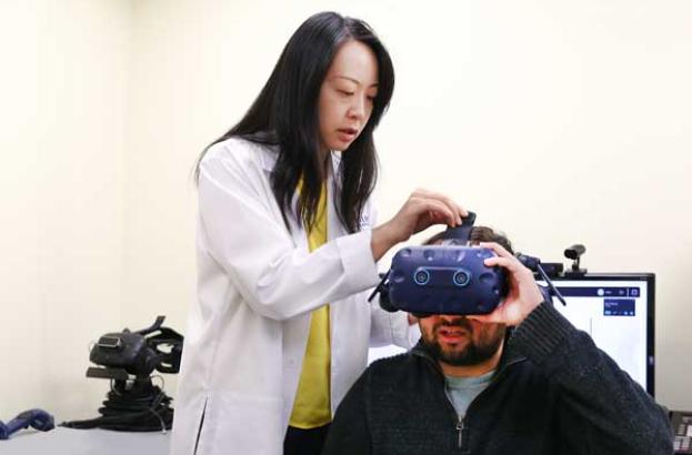 Peii Chen, PhD, senior research scientist at Kessler Foundation, placing a virtual reality headset on a participant