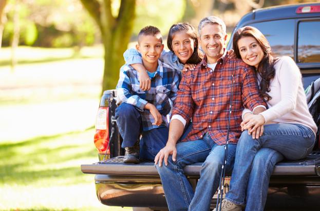 hispanic Family Sitting In Pick Up Truck On Camping Holiday