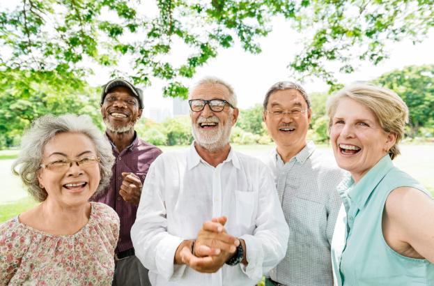 A small group of adults standing close together outdoors, smiling and posing for a group photo with trees and greenery in the background.