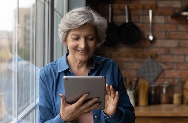 Individual using a digital tablet near a bright window, representing participation in a multiple sclerosis research study through online enrollment. 