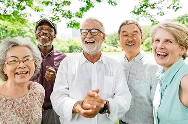 A small group of adults standing close together outdoors, smiling and posing for a group photo with trees and greenery in the background.