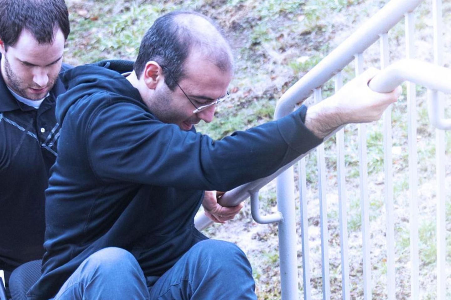 man helping another man in a wheelchair go up the stairs