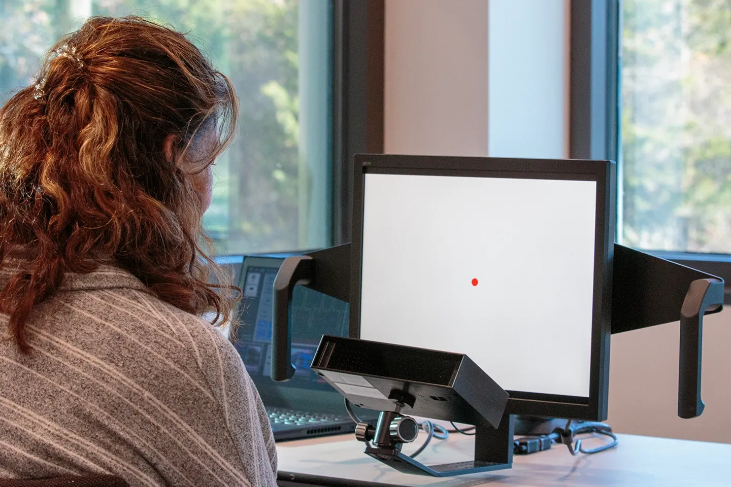 Woman views a computer screen that shows a red dot in the center as point of reference.