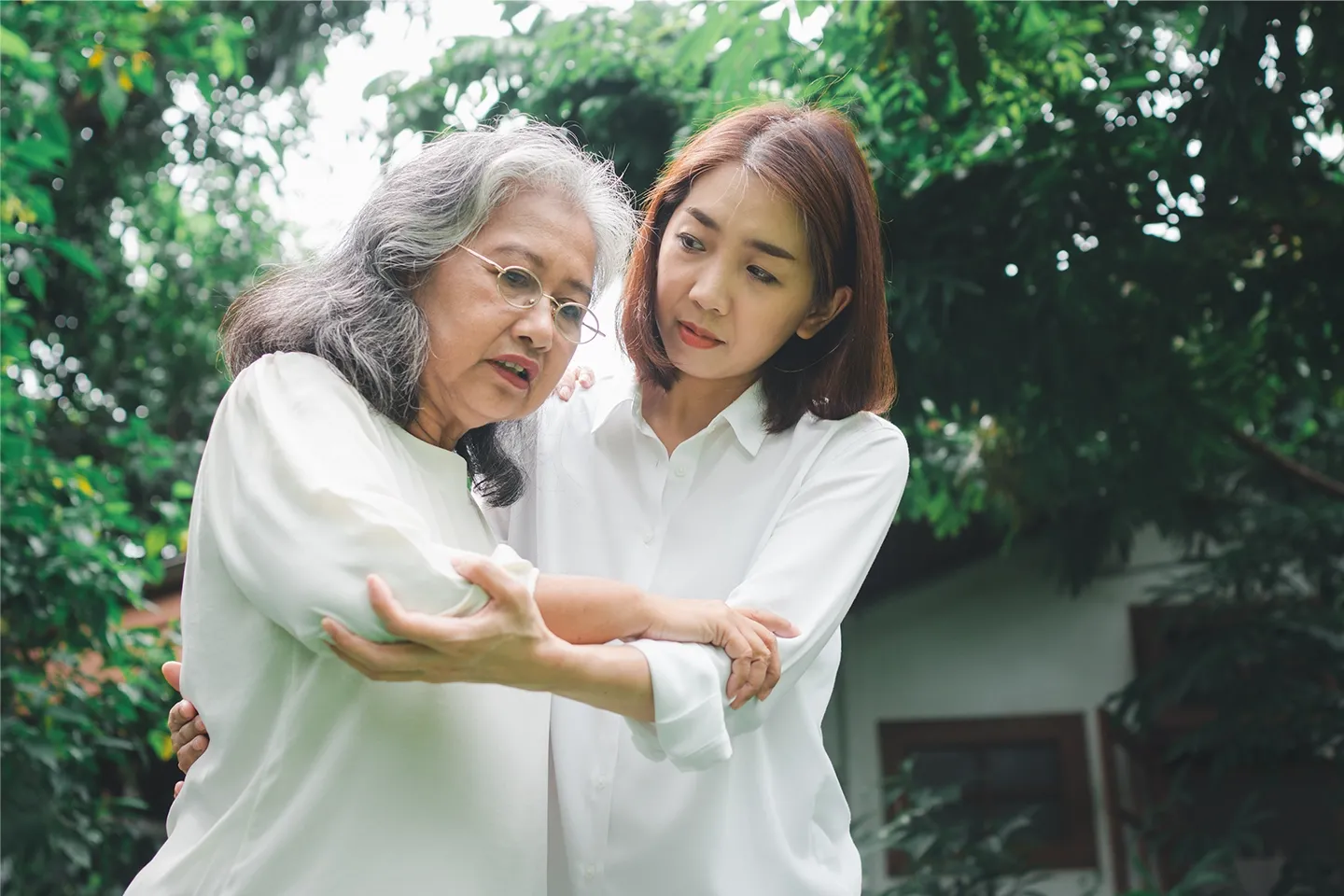 Two Asian woman, younger one holding arm of older one to help her walk