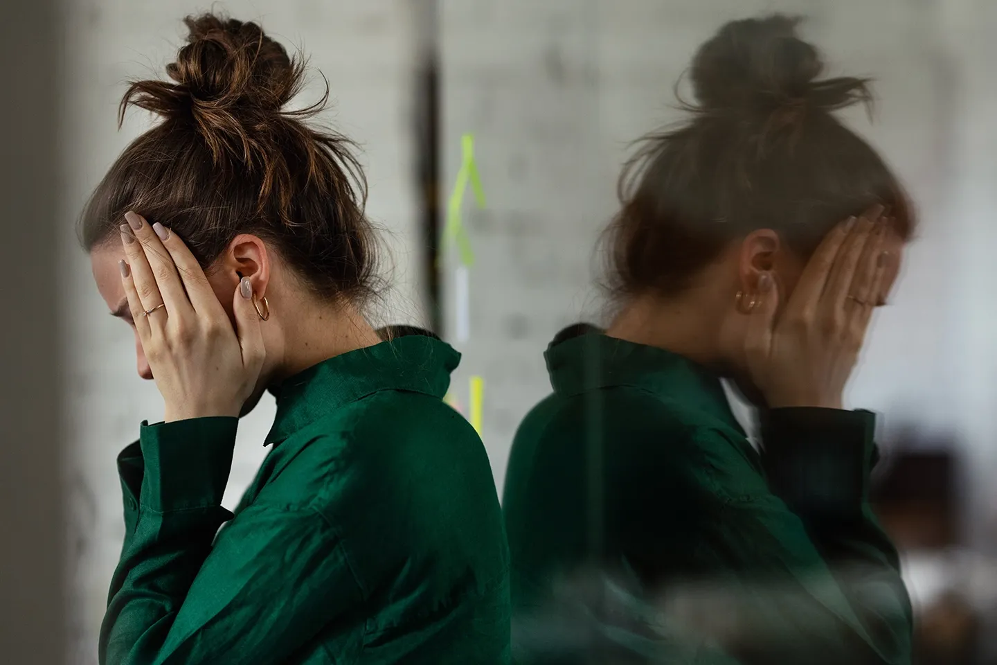 Picture of white female stressfully holding both sides of her face, reflected in a mirror.
