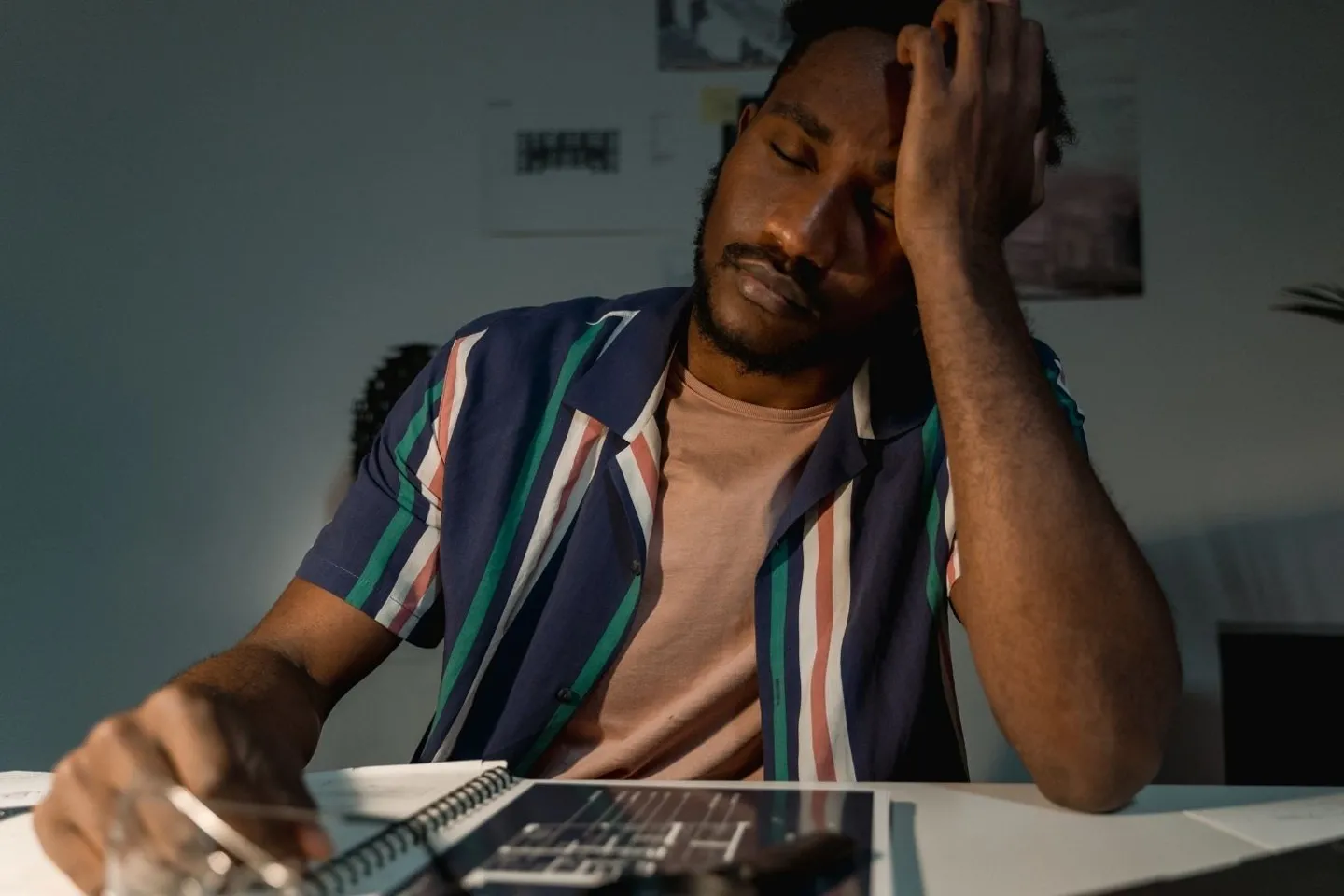 A man seating at a desk with his hand on his face