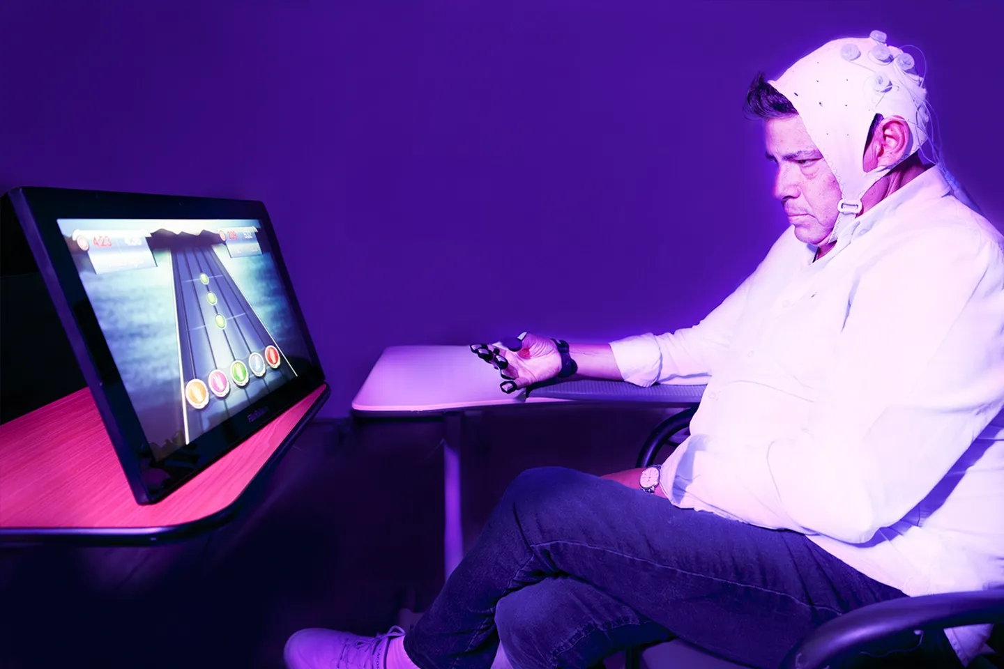 A stroke participant performing rehabilitative hand exercises while sitting in front of a computer screen that shares a gaming element to make the exercises more interactive.