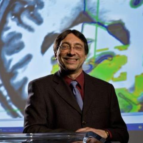 Head shot of Dr. John DeLuca against a colorful background with a brain 