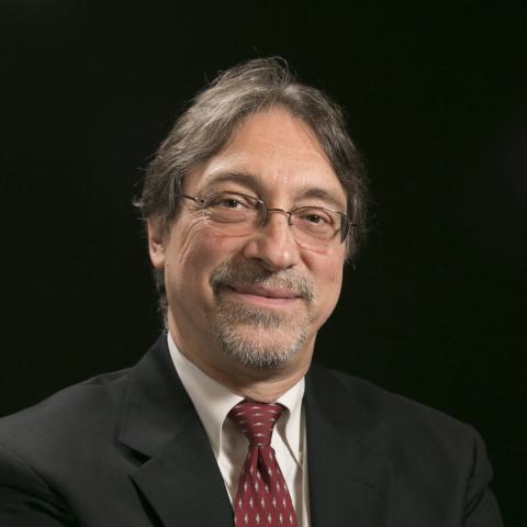 Dr. John DeLuca hands folded wearing a suit