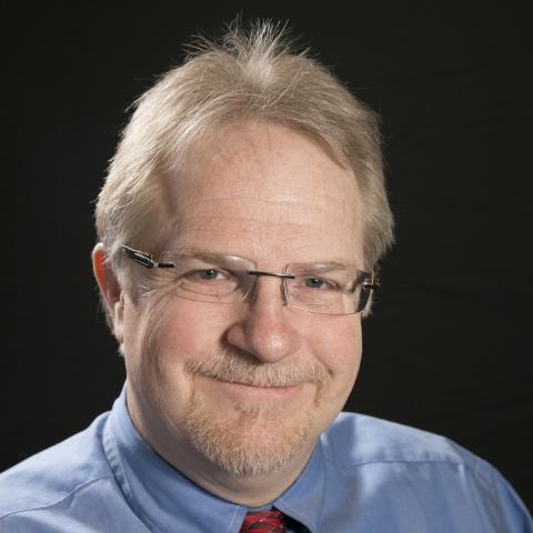 Dr. Trevor Dyson-Hudson wearing a blue shirt and red tie