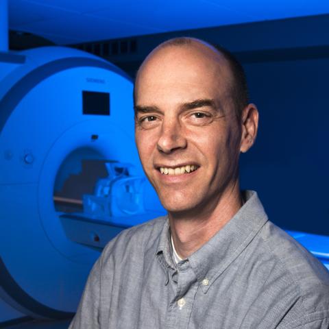 Headshot of Dr. Glenn Wylie standing near a MRI Scanning machine