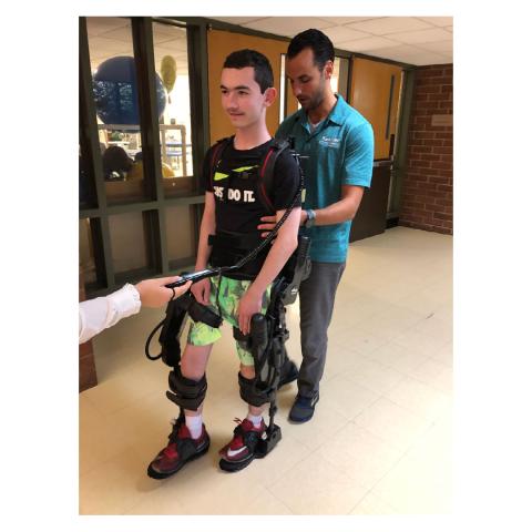 Two males, one is a young adult walking with an exoskeleton
