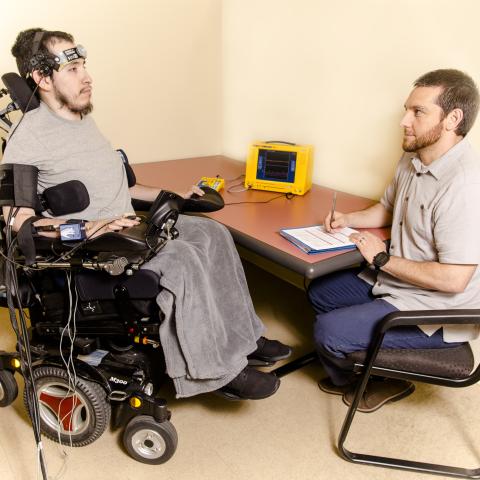 Photo of participant in a wheelchair, while researcher takes notes