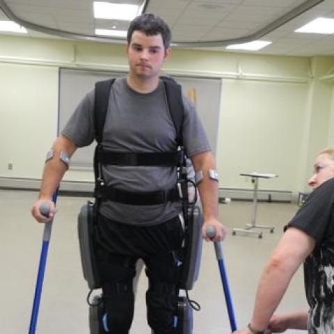 man wearing a grey shirt using a ekso walking robotic mechanism for spinal cord injury.