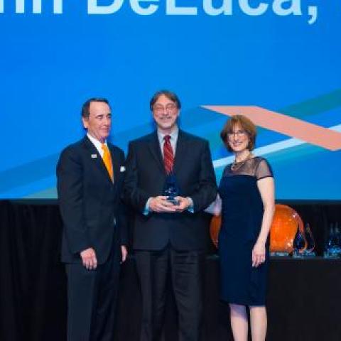 award picture of two men in suits and a woman in a blue dress